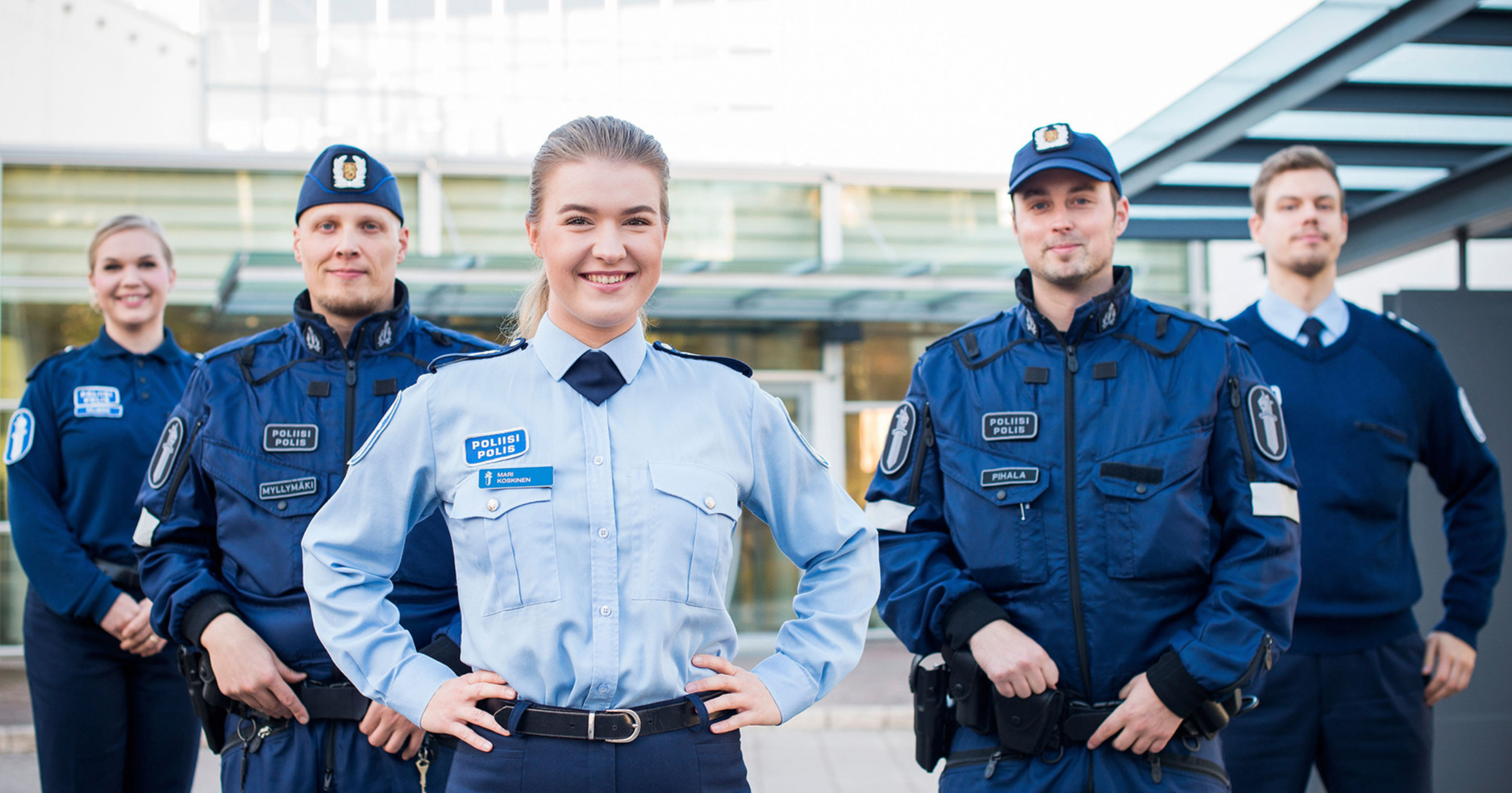 Five smiling police students in uniform standing in the courtyard of the Police University College.