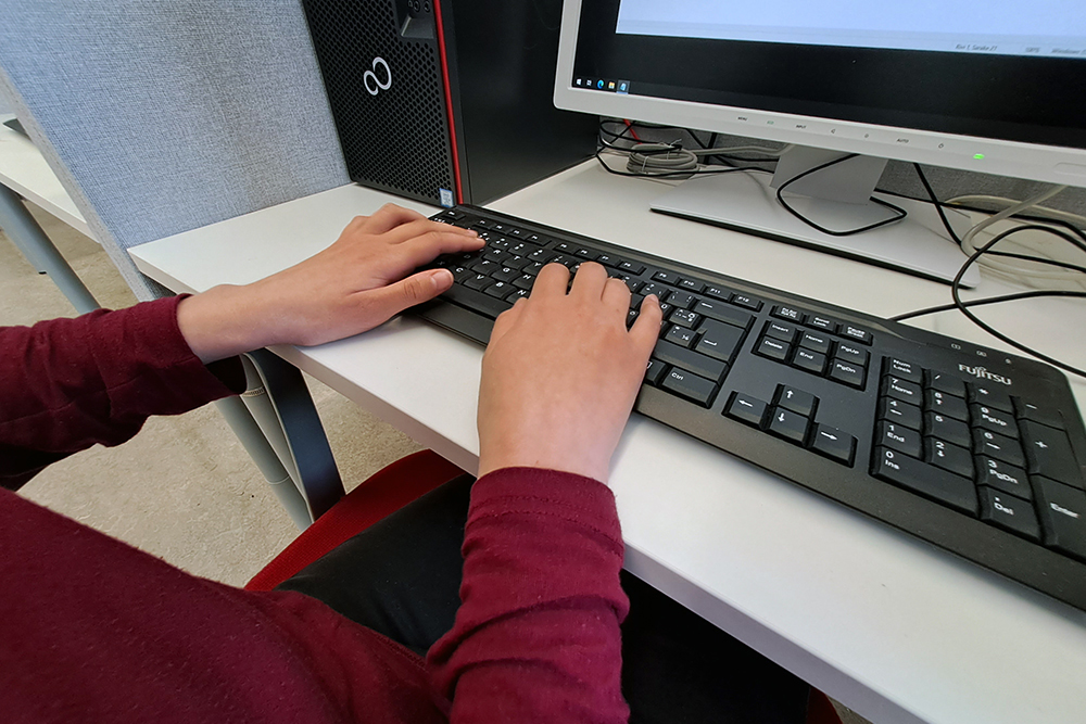 Händerna på datorns tangentbord, längst bak syns nedre delen av datorns skärm.