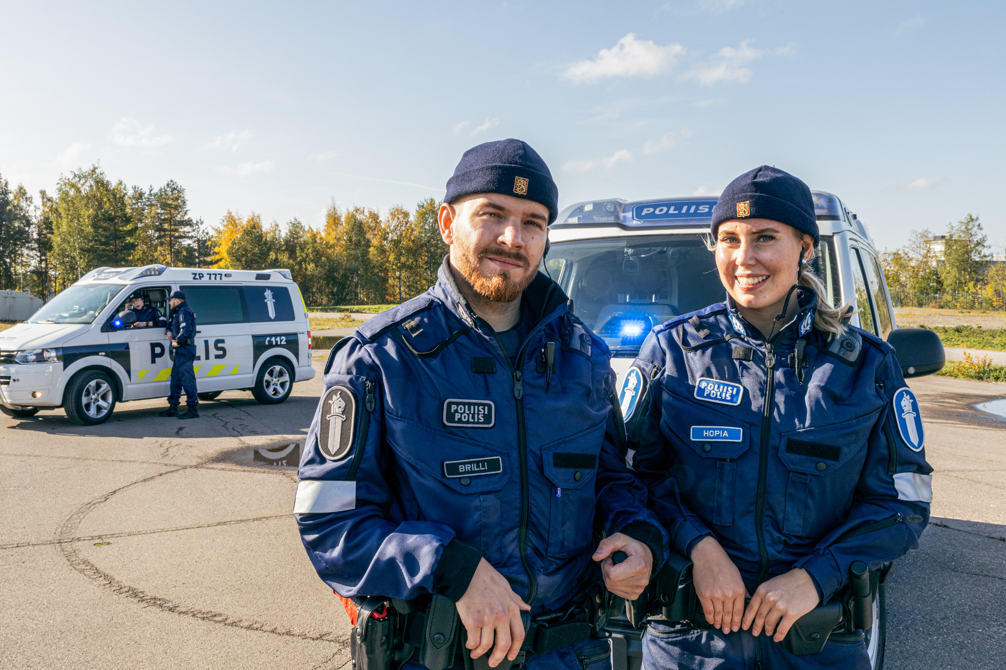 Två polisstuderande i uniform  på Polamks körövningsbanan, med två polisbilar och två polisstuderande i bakgrunden.