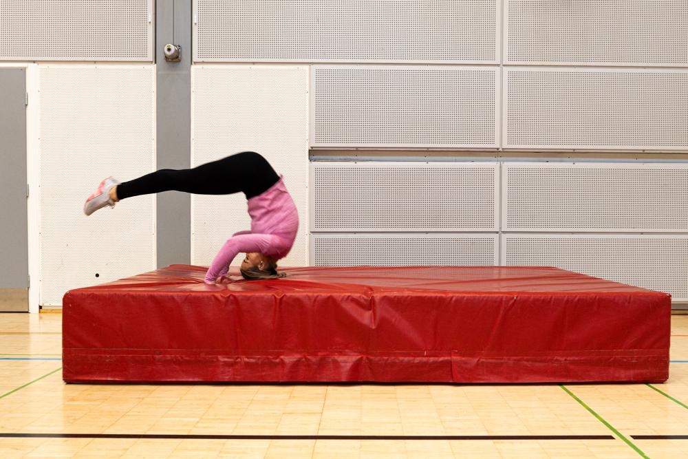 En sökande gör en kullerbytta på den tjocka madrassen i gymnastiksalen.