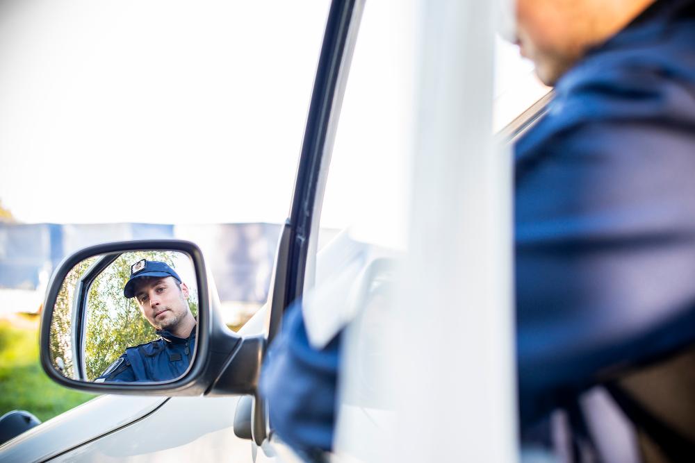 A uniformed police student in a police car taking a look in the side mirror.