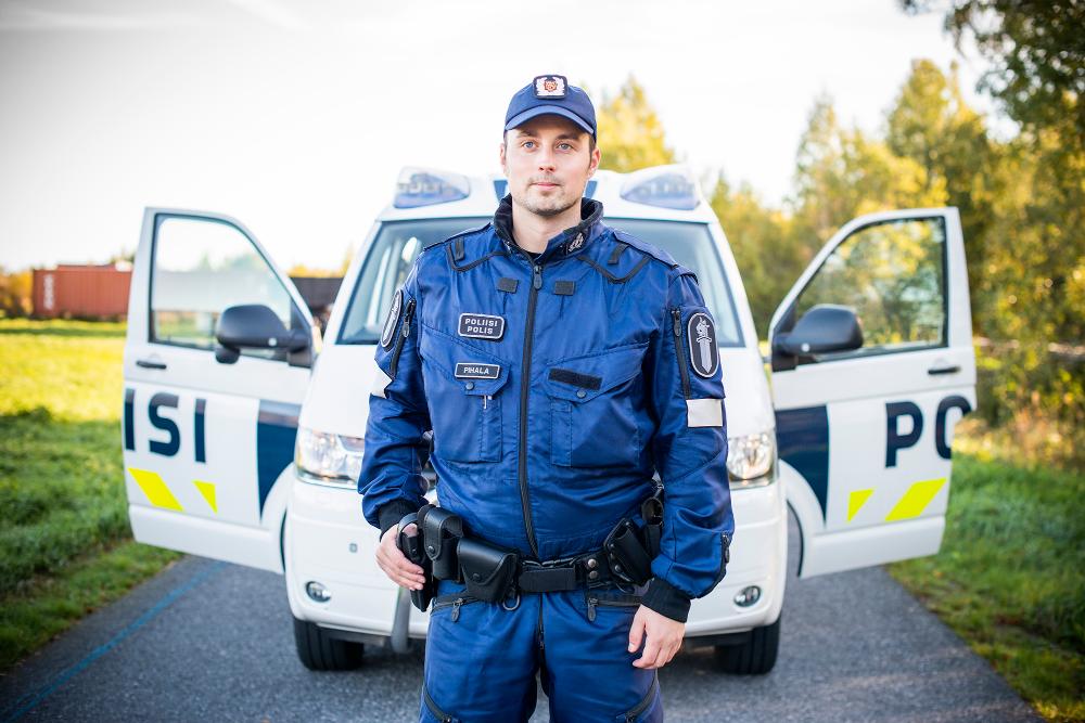 En polisstuderande i uniform står på en väg framför en polisbil med öppna framdörrar.