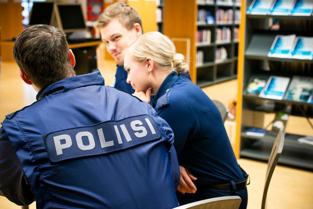 Tre polisstuderande i uniform vid ett bord i biblioteket.