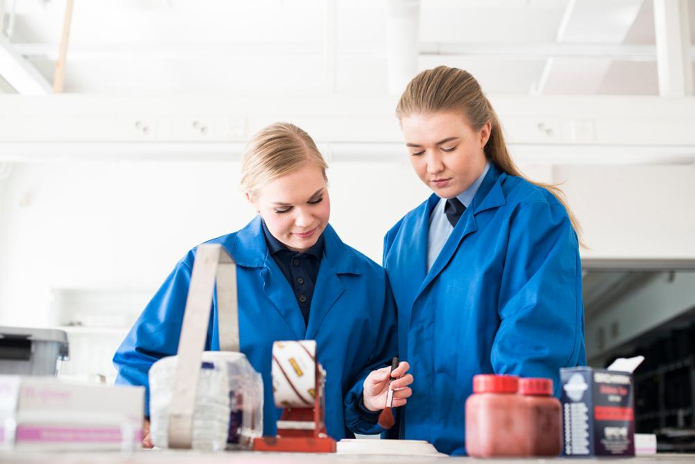 Kaksi sinisiin laboratoriotakkeihin pukeutunutta opiskelijaa Polamkin teknisen rikostutkinnan laboratoriossa.