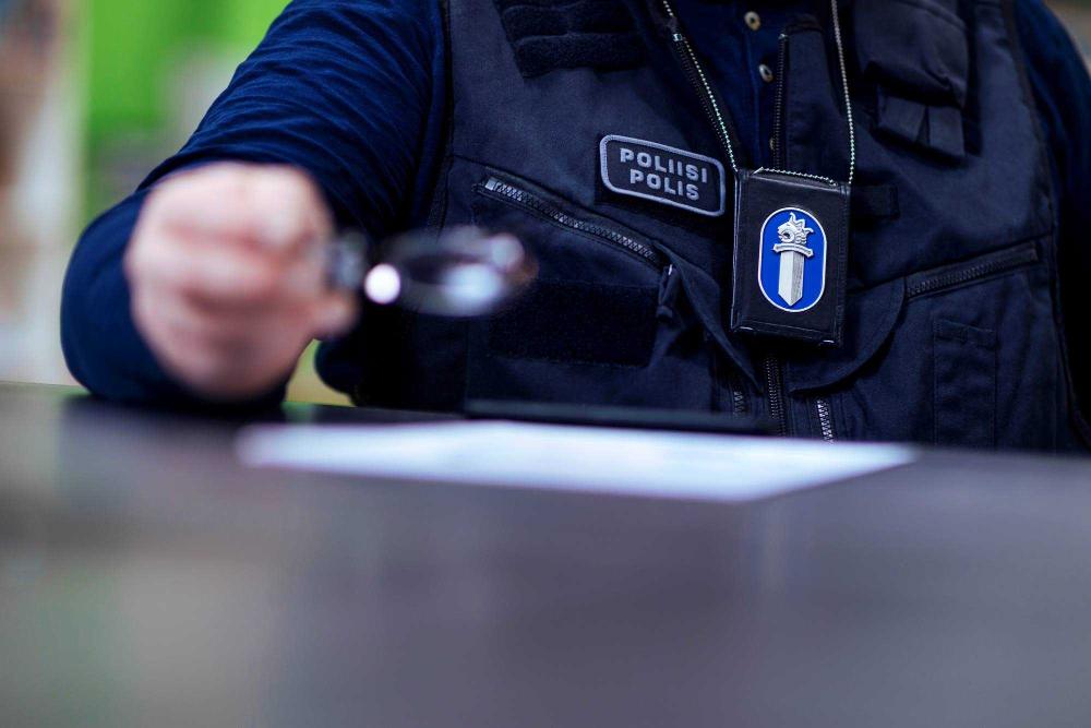 En polis med polisens tjänstemärke i sitt fodral runt halsen står invid ett bord.