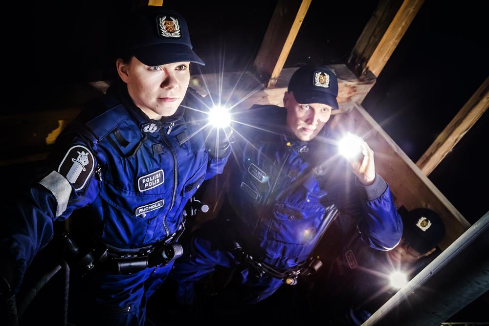 Two uniformed police students with torches in a dark storehouse. 