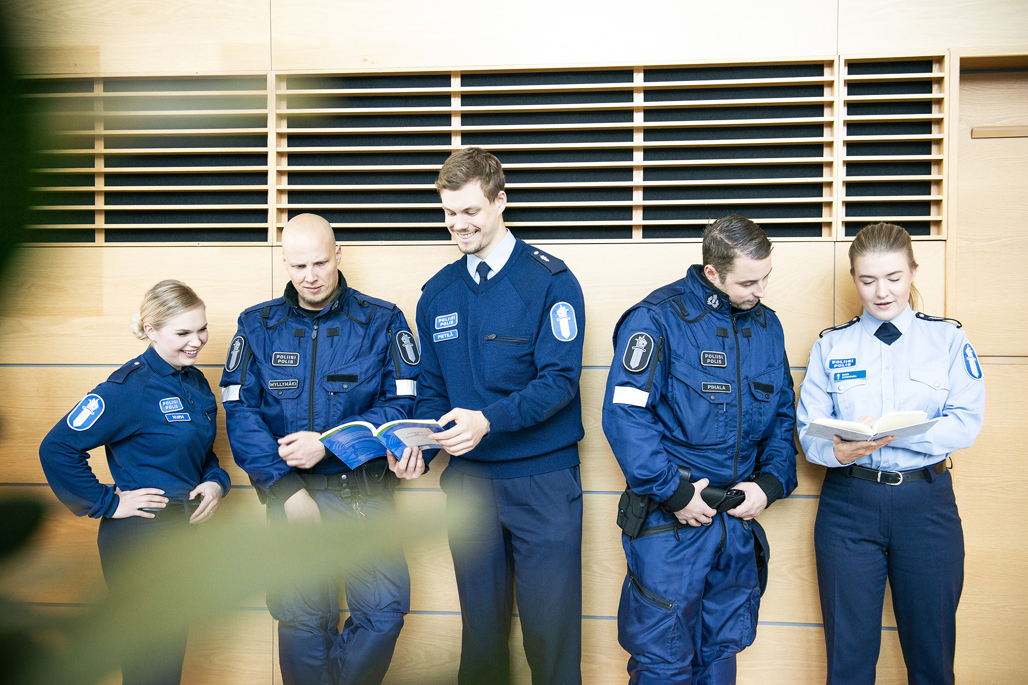 Fem studerande i uniform på rad i aulan tittar på böcker.