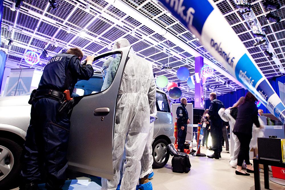 En polisstuderande i tjänsteuniform tillråder mässbesökarna i en brottsutredningsuppgift. De som utför uppgiften klär sig i vita overaller och söker ledtrådar från en personbil.