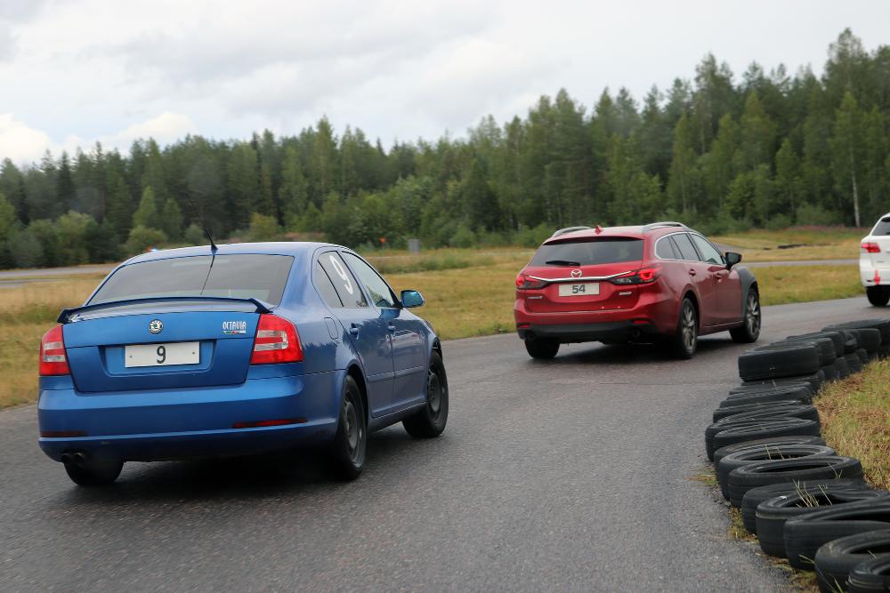 Three cars with numbered signs instead of registration plates driving in a line on an asphalt track. 