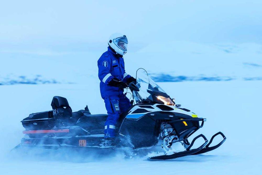 A police officer driving a snowmobile in winter in an upright position. 