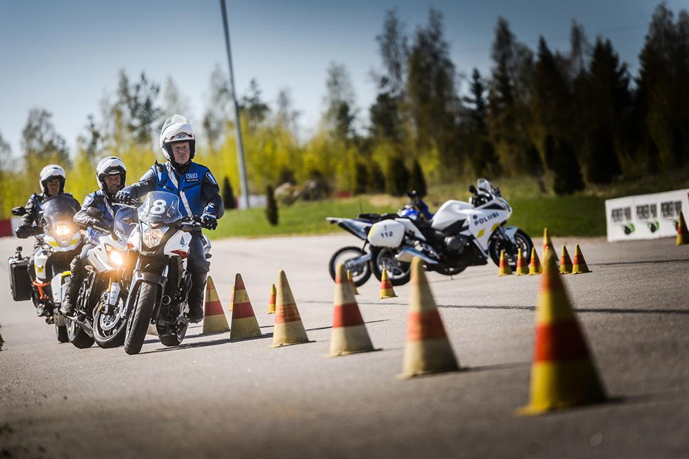Motorcycle police weaving between the cones laid out on an asphalt track.