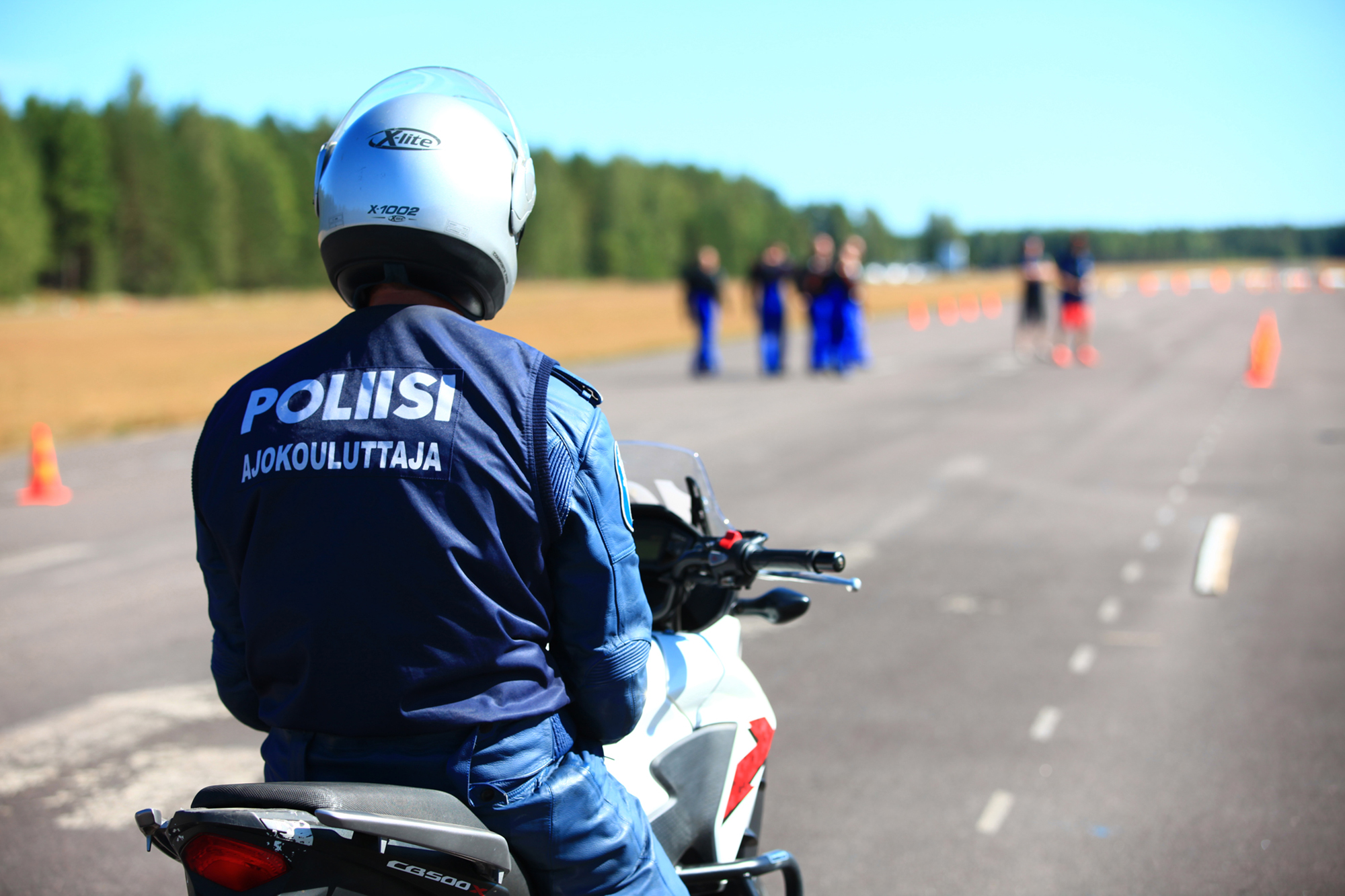 Ajokouluttaja poliisimoottoripyörän päällä selkä kameraan päin, taustalla ajorataa.