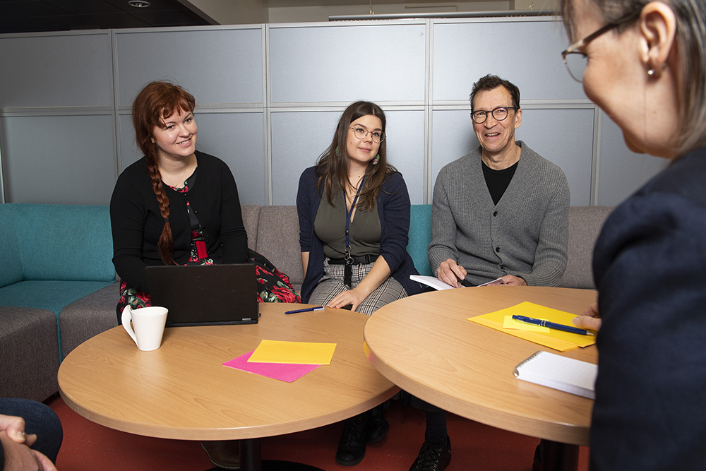 Four persons are working together at a desk.